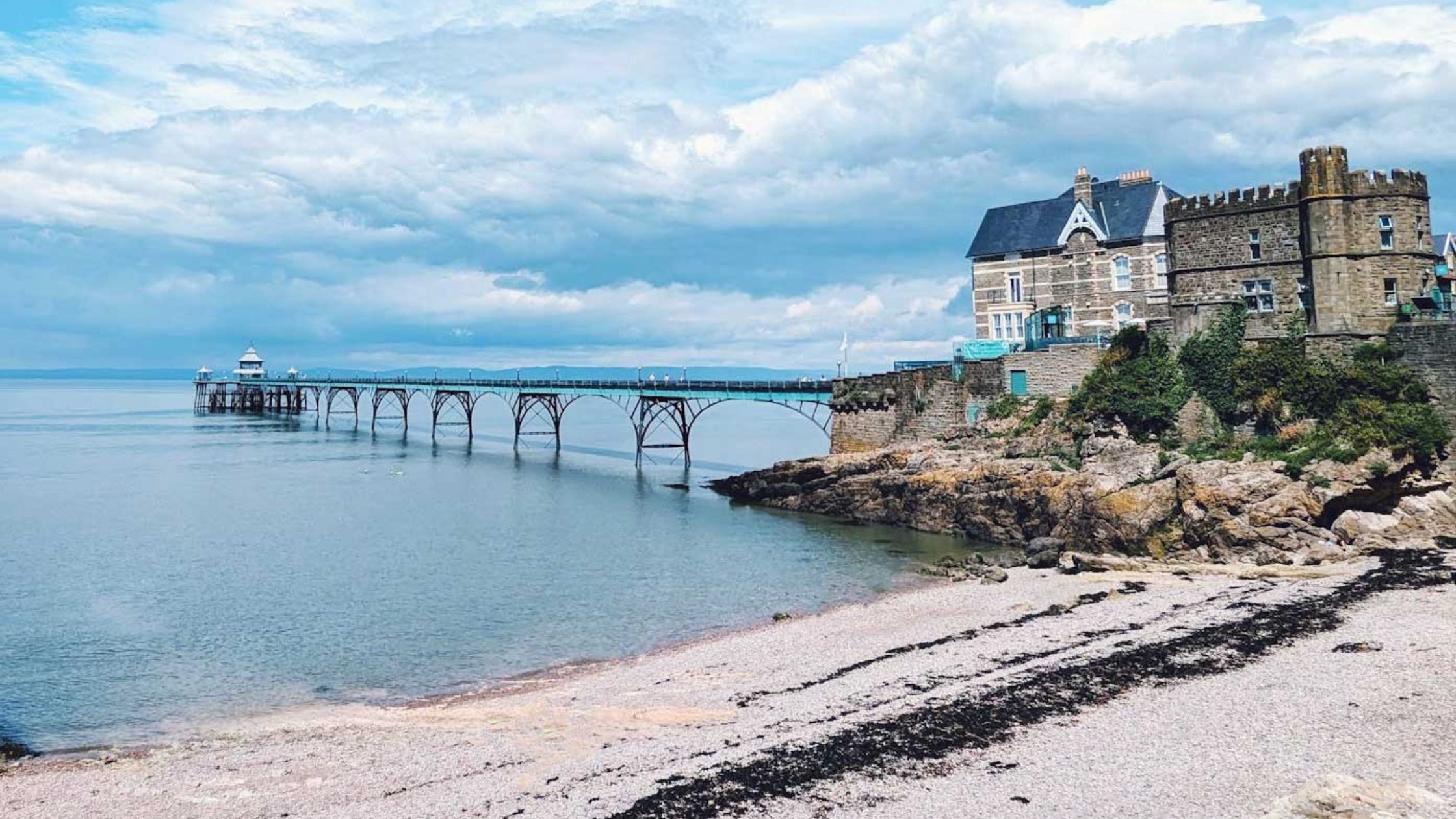 Blue metal pier in Clevedon with small beach and houses on the hill